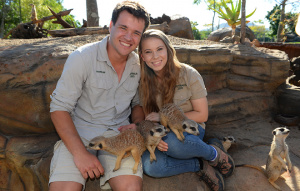 Bindi Irwin and Chandler Powell sitting with meerkats on their lap.